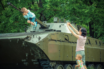 Mom takes pictures of his son on vintage military vehicle.