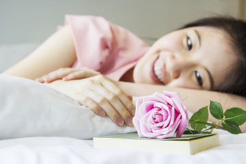 Cute young woman with rose on the bed at home