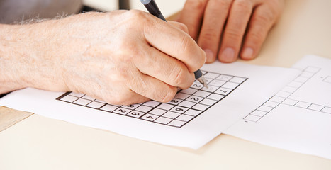 Hände eines Senioren lösen Sudoku Rätsel