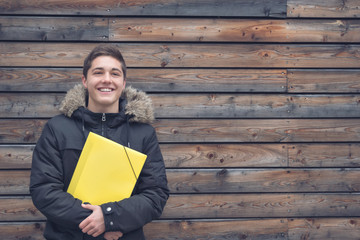 Schüler mit gelber Mappe lachend vor Holzwand