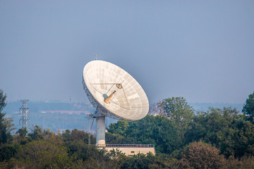 Large satellite dish on the forest over clouded background