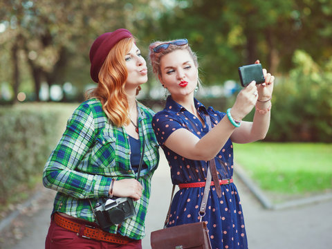 Two beautiful hipster girls taking pictures of themselves on mob