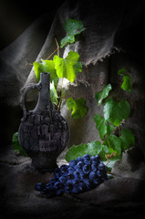 Wine in a clay bottle and grape leaves on background of burlap