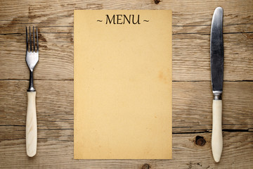 Blank menu, fork and knife on old wooden background
