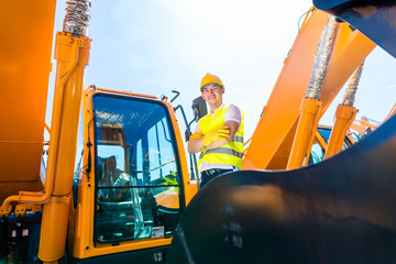 Asian builder in excavator on construction site © Kzenon