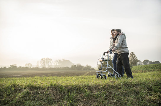 Senior man and grandson in rural landscape with wheeled walker