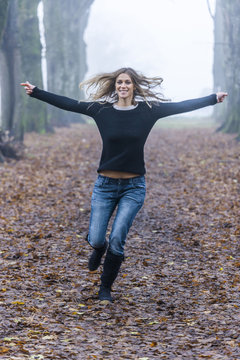 Woman with outstretched arms running along a forest track