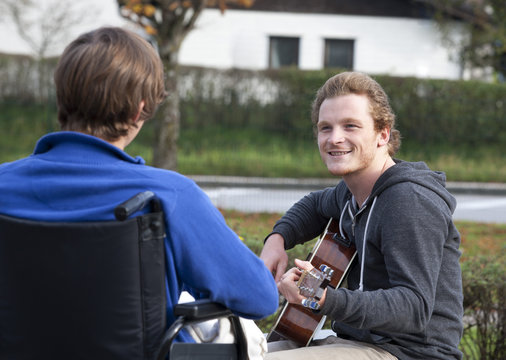 Young wheelchair user listening guitarist