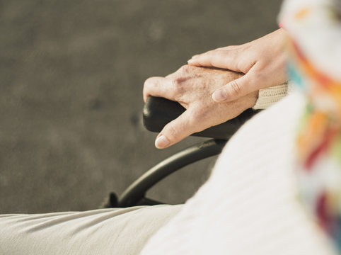 Young woman's hand on hand of senior woman sitting in wheelchair
