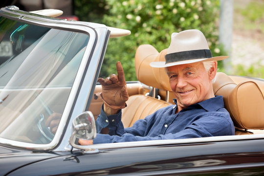 Fototapeta Portrait of a smiling senior sitting in a convertible car waving