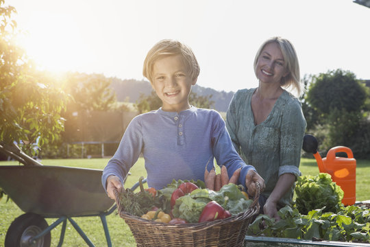 Boy with mother in garden carrying basket with vegetables