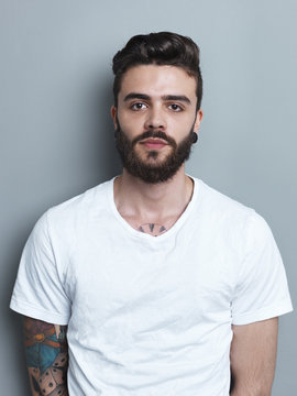 Portrait of tattooed brunette man in front of gray background