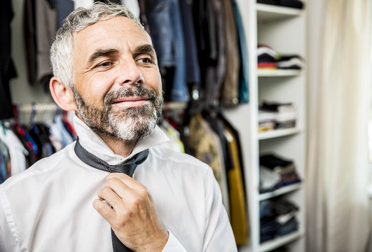 Portrait of smiling businessman binding tie at his walk-in closet