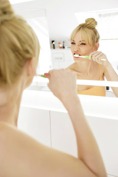 Woman looking at her mirror image while brushing teeth