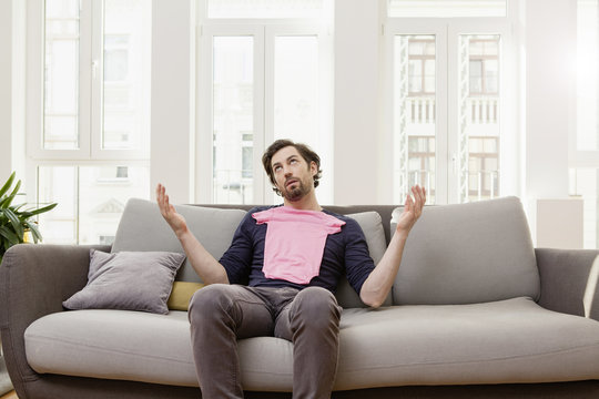 Disappointed man with pink baby shirt on couch