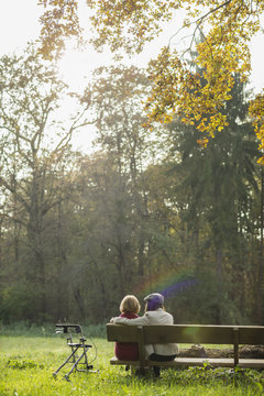 Senior woman and granddaughter sitting on a park bench, back view