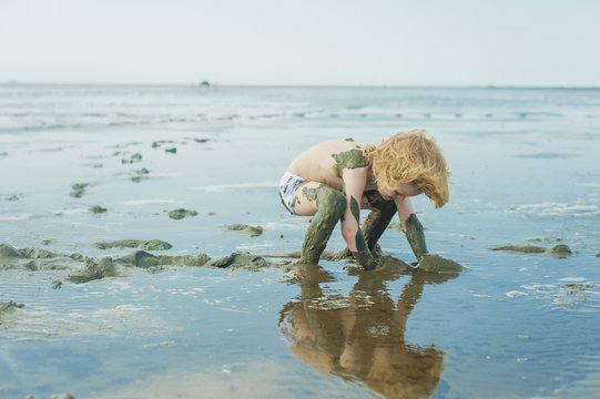 Germany, Schleswig Holstein, Boy playing in mud at beach