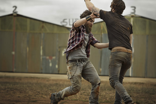 Two men with full beards fighting in abandoned landscape