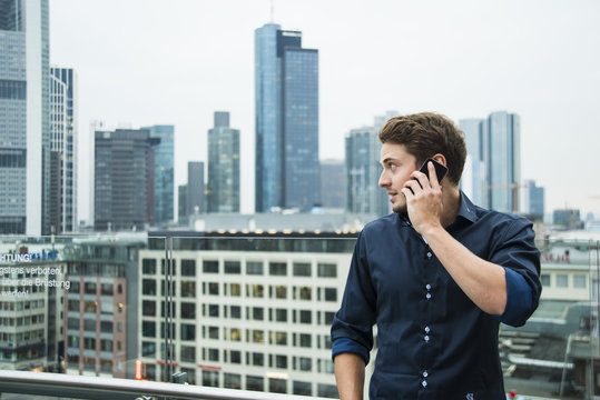 Germany, Hesse, Frankfurt, young man telephoning with his smartphone in front of the skyline
