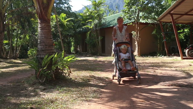 grandmother carries blonde toddler in pram	