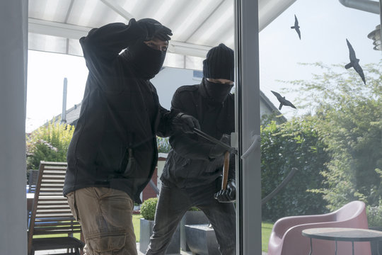 Two burglars opening terrace door of an one-family house with hammer and crowbar at daytime