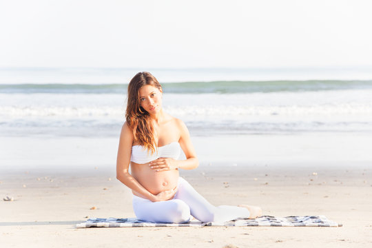 Schöne, schwangere Frau sitzt am Strand