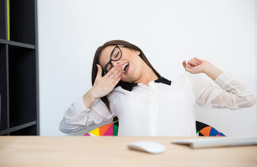 Young businesswoman sitting at her workplace and yawning