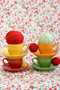 Four colorful cups and balls of yarn on a background