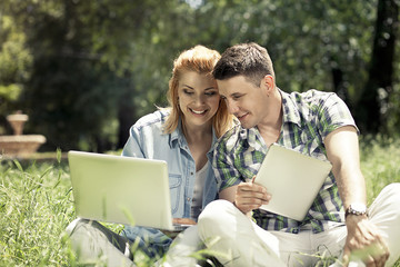 Young attractive couple sitting on the grass, looking at laptop