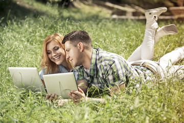 Young attractive couple lying on the grass, looking at laptop an