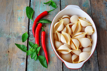 pasta shells in ceramic form, chili pepper and basil on a wooden