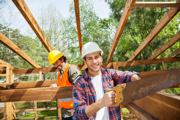 Happy Worker Cutting Wood With Handsaw At Construction Site