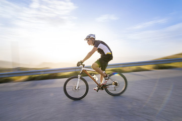 Obraz premium Cyclist man riding mountain bike in sunny day on a mountain road