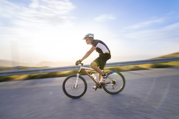 Cyclist man riding mountain bike in sunny day on a mountain road