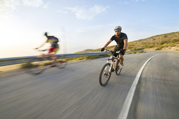 Fototapeta premium Cyclist man riding mountain bike in sunny day on a mountain road