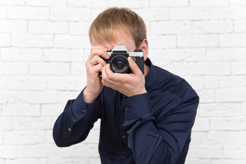 Elegant young man with old rare photo camera on white brick back