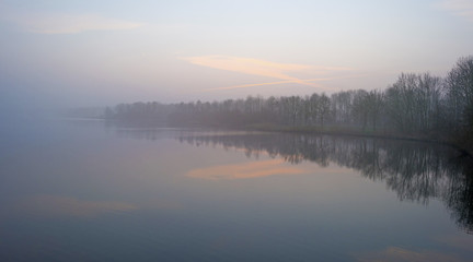 Obraz premium The shore of a foggy lake in winter at dawn