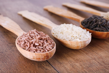 Different kinds of rice in spoons on wooden background