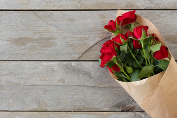 Red roses wrapped in paper on wooden table background