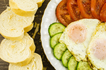 Fried eggs with bread, tomato and cucumber on plate