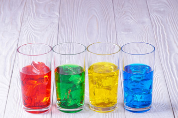 glasses with colored water and ice on a white wooden fonne