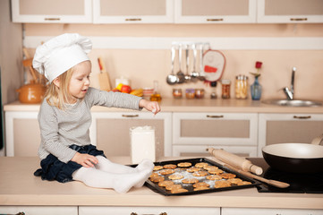 Little cute girl with chef hat preparing cookies in kitchen