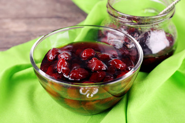 Tasty jam in jar and bowl with napkin on table close up