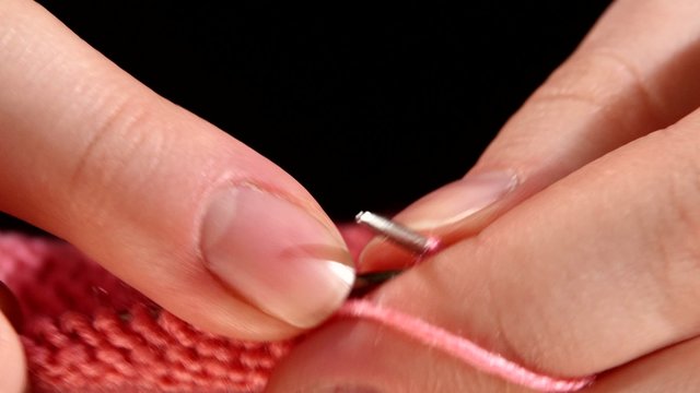 Woman sits and knits pink scarf fine knit, close up