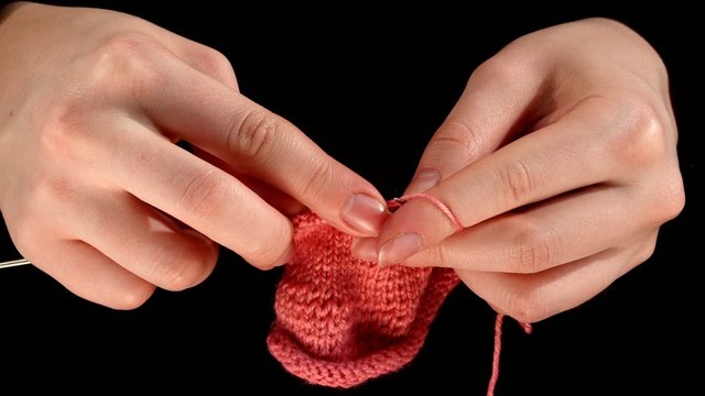 Woman sits and knits pink scarf, fine knit on black background