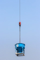 Obraz premium blue cement bucket is lifting on crane hook in construction site