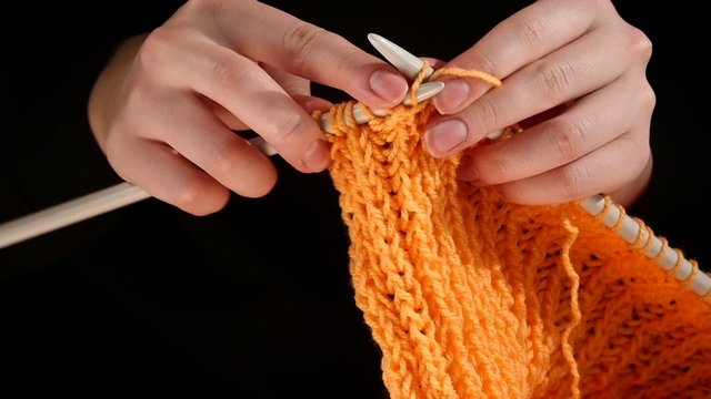 Woman sits and knits orange scarf, large knit, on black