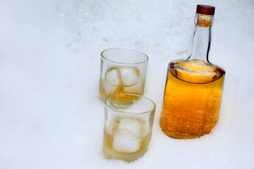 Bottle of whiskey with two glasses in the snow