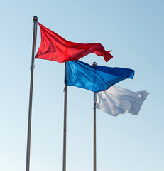 White, blue and red flags against sky.