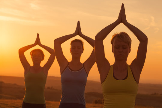 Three girls practicing yoga in sunset